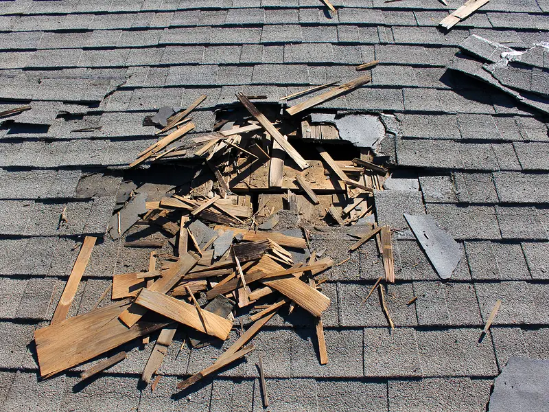Asphalt shingle roof with torn shingles and storm debris